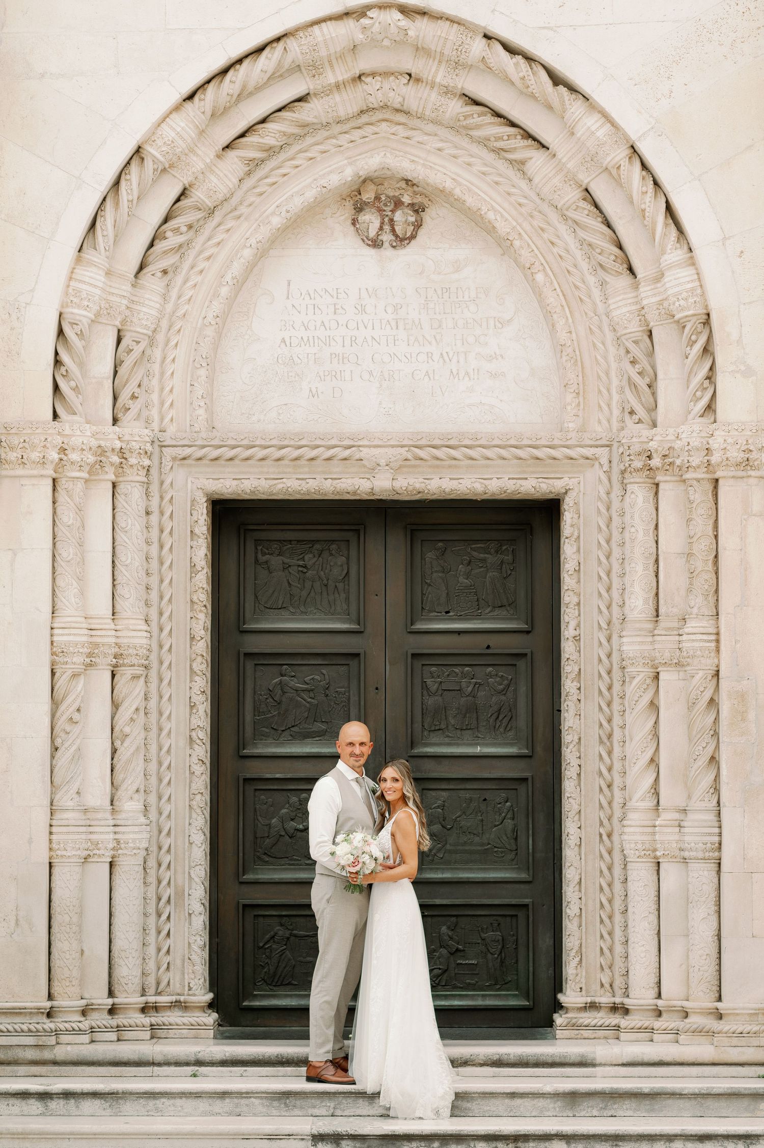 Wedding portrait under a beautifully carved stone archway with ornate dark wooden doors.