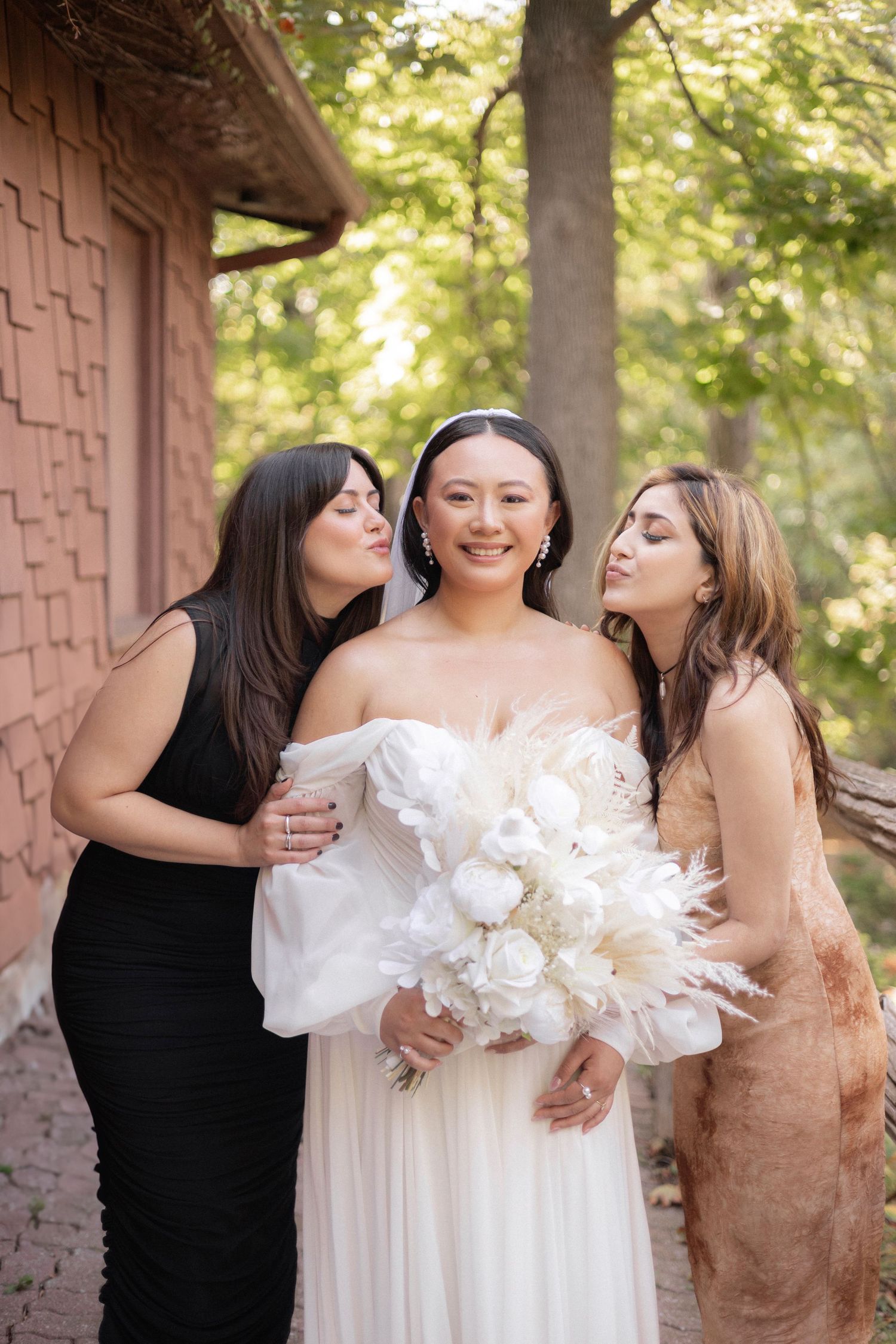 Wedding celebration moment with bride in white gown joined by two friends in dark and neutral dresses.
