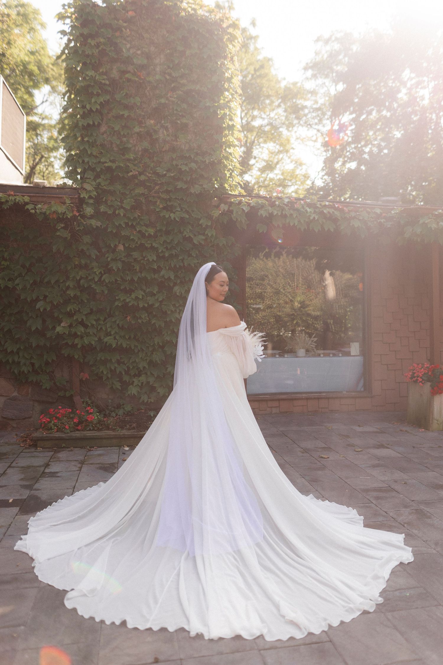 Back view of a wedding dress with long train on stone patio with ivy-covered walls.