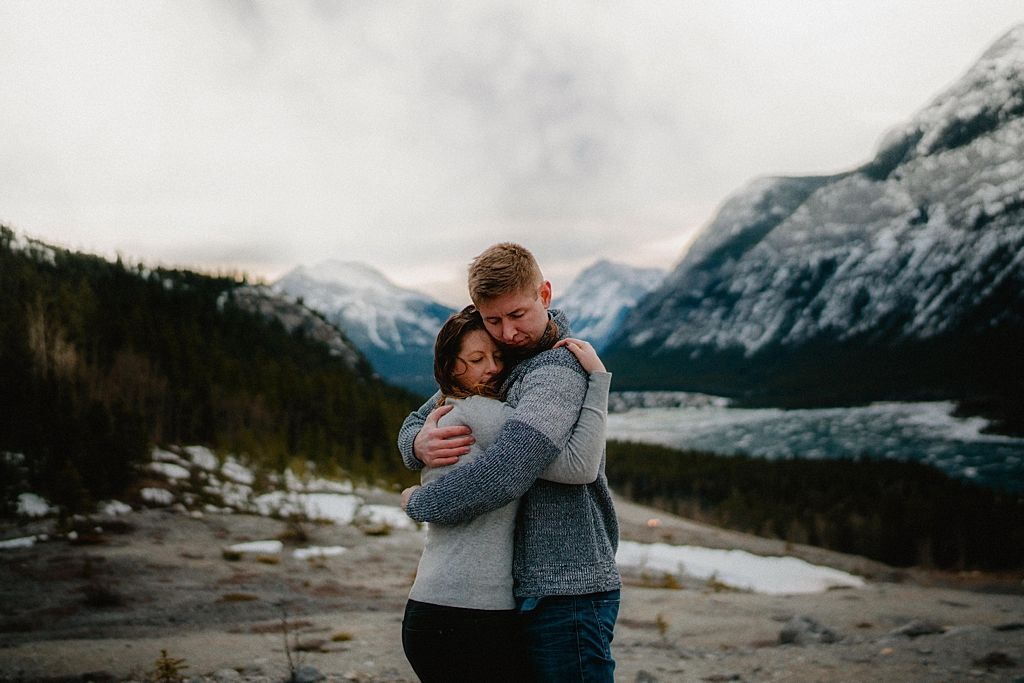 Intimate embrace between couple against dramatic mountain landscape with winter snow.