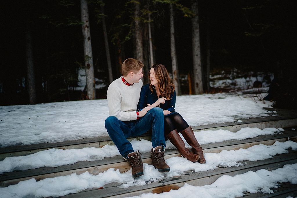 Couple sitting together on snowy log in winter forest setting.