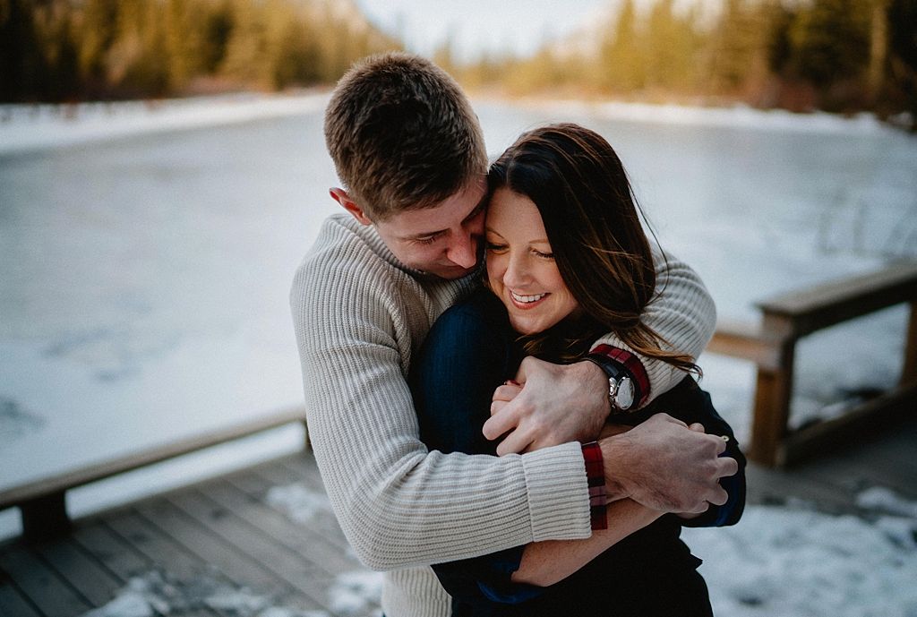 Sweet embrace shared on wooden deck with snowy lake and forest backdrop.