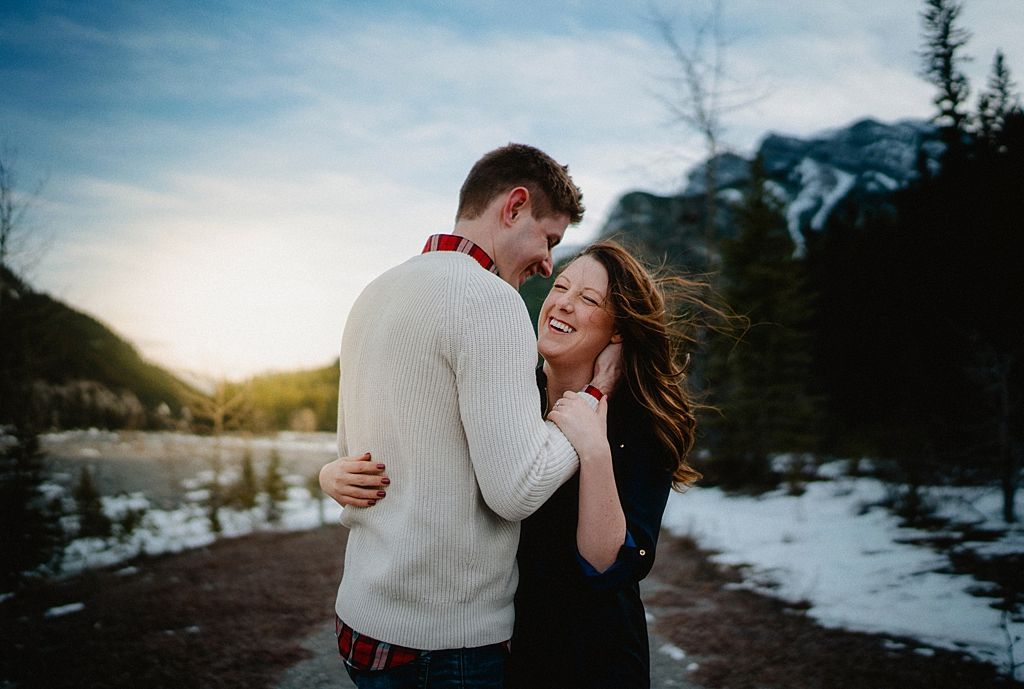 Tender moment between couple laughing together in winter mountain landscape at golden hour.
