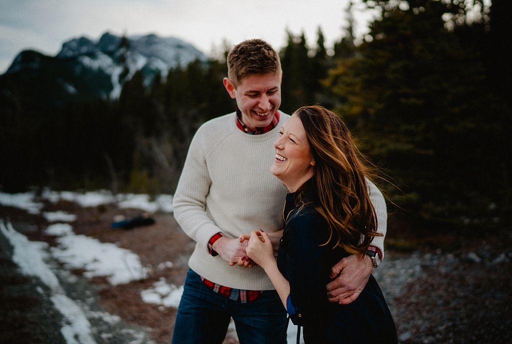 Candid moment of couple laughing together on snowy mountain trail during winter.