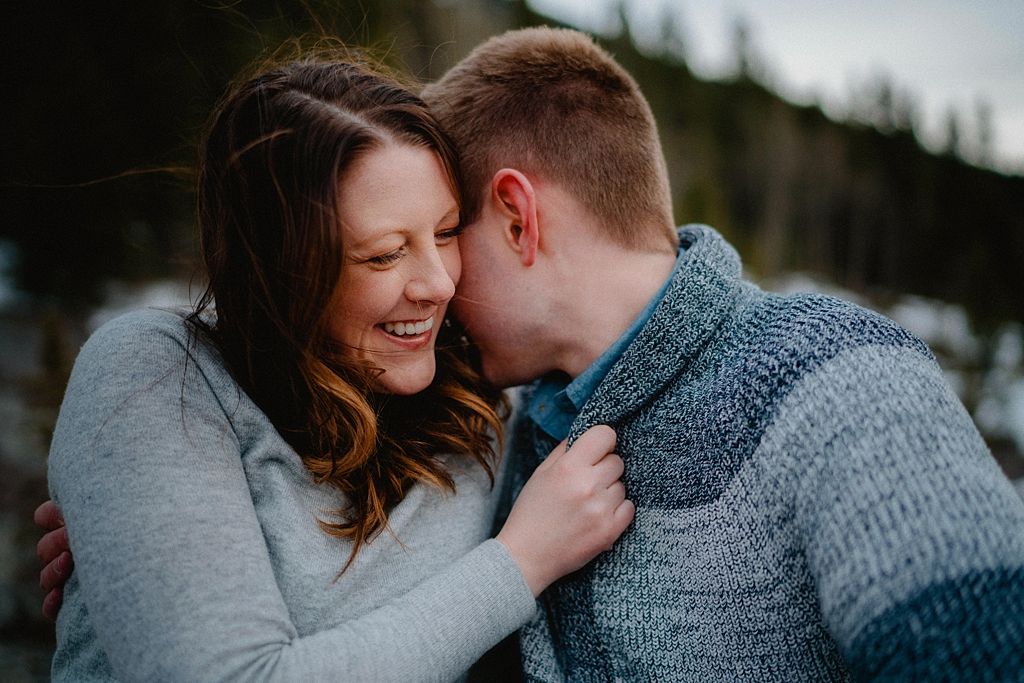 A tender moment of laughter shared between two people wearing cozy sweaters in a mountain setting.