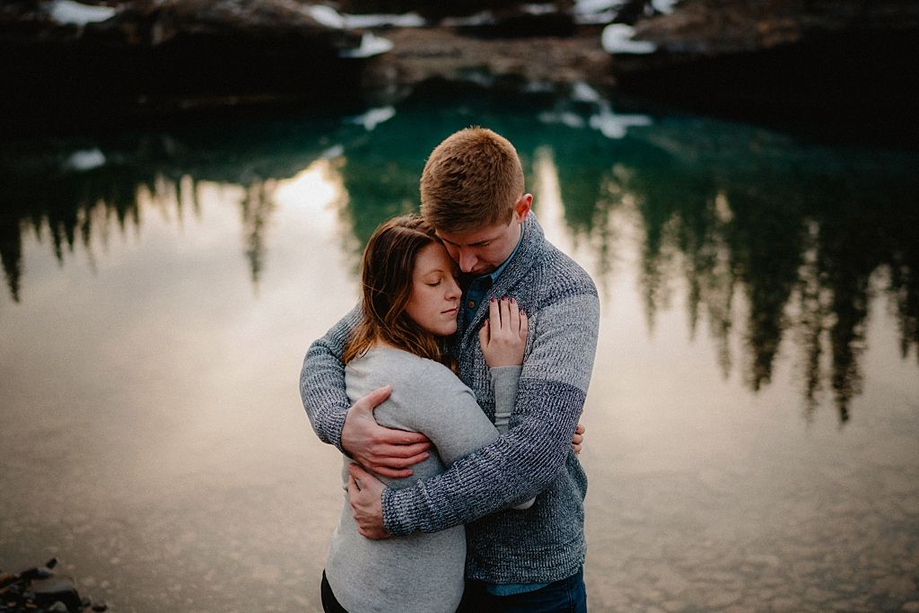 A tender moment shared beside a reflective mountain lake with turquoise waters.