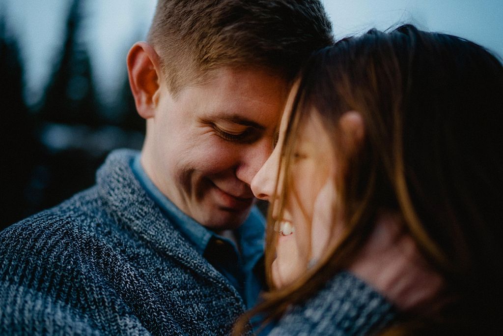 A tender winter moment captured between two people in a snowy forest setting.