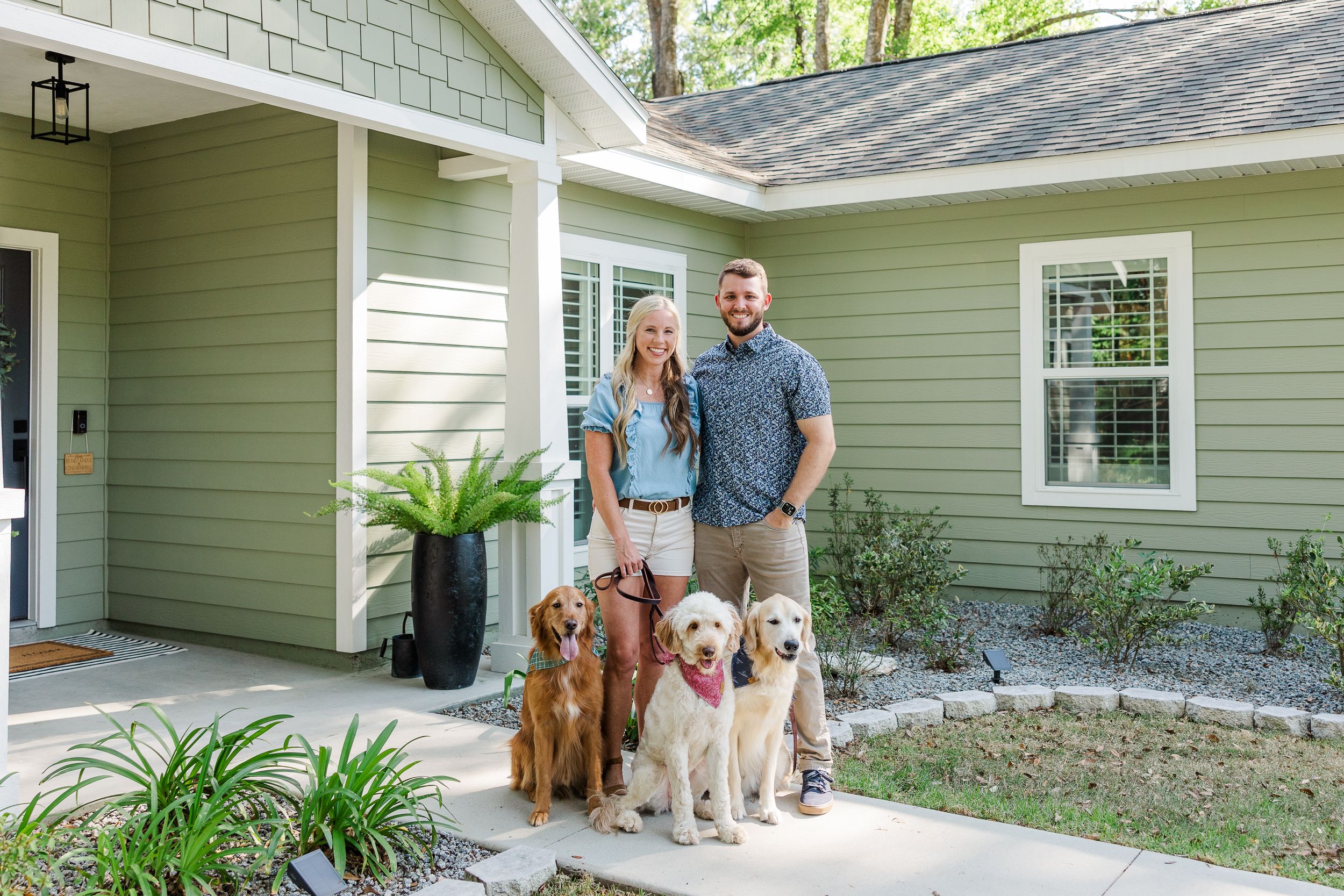 Modern sage green house exterior with white trim and family pets in the driveway.