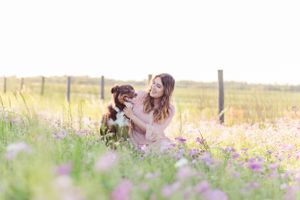 Dog and owner sitting in field of wildflowers during golden hour.