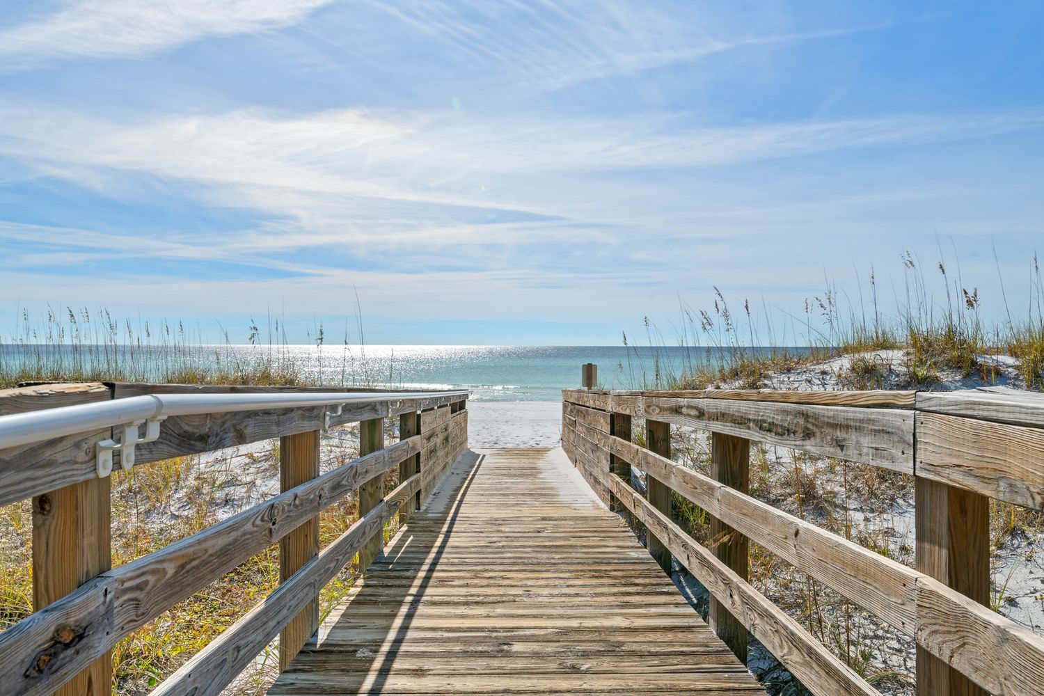 Wooden boardwalk leading to beach with sea oats and blue sky.