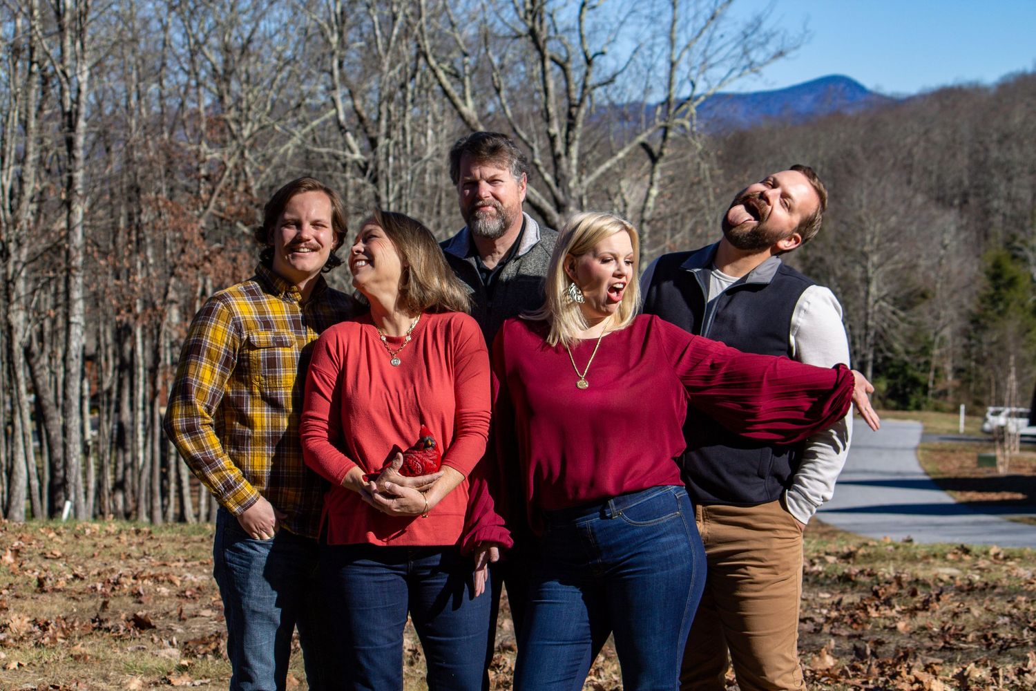 A group of friends laughing together outdoors with autumn trees in the background.