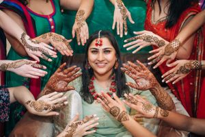 Indian bride surrounded by hands with henna designs during mehndi ceremony in Redondo Beach, California