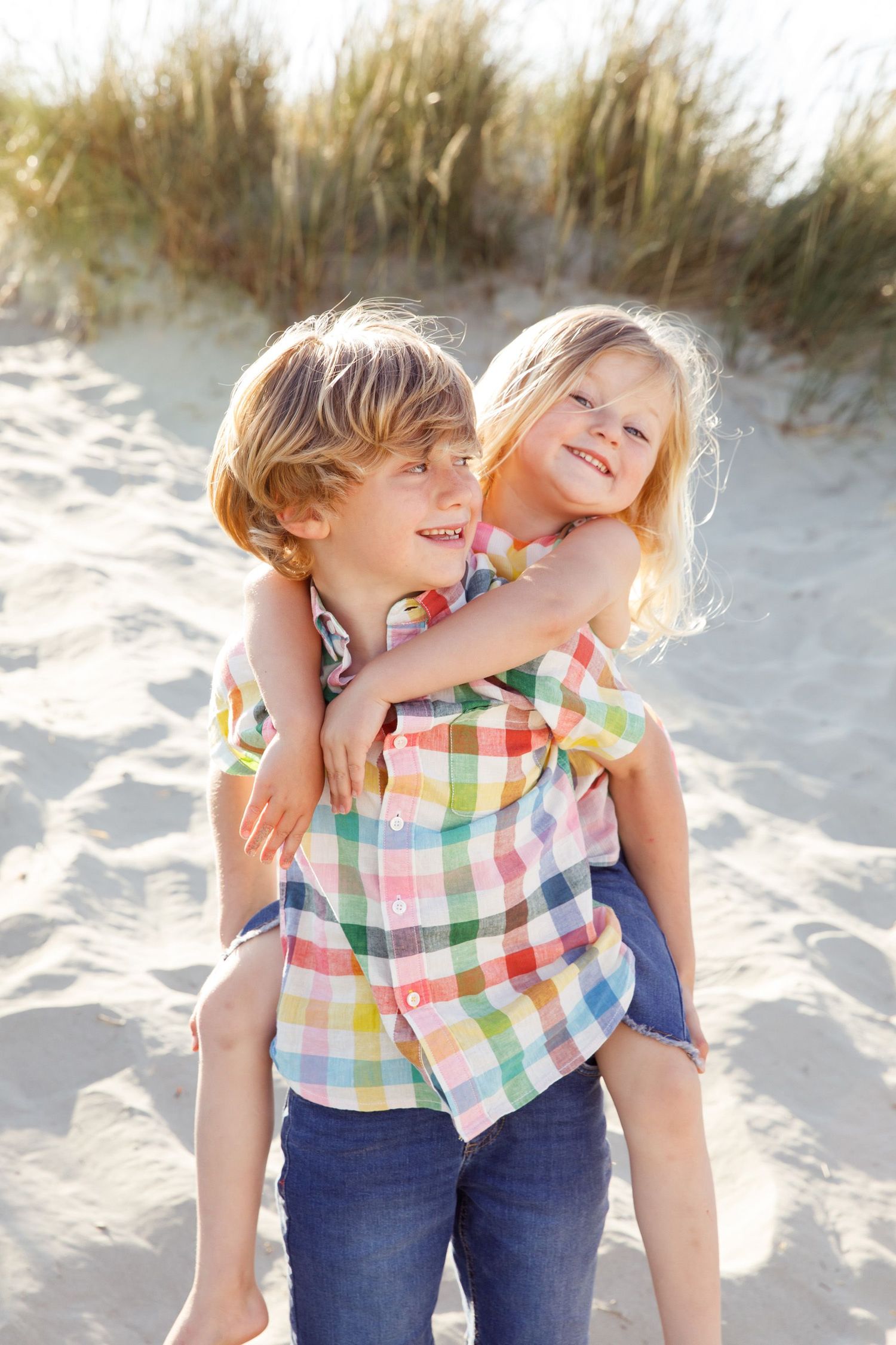 Two children playing and laughing together in sandy beach dunes.