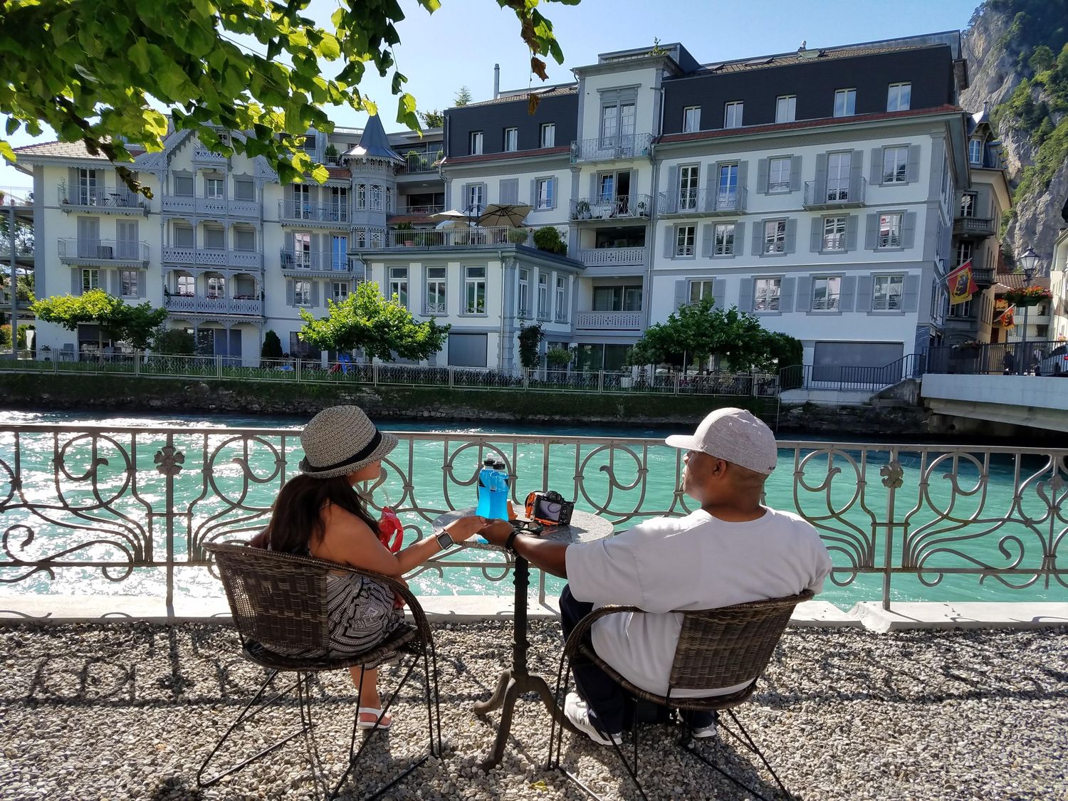 Couple relaxing by a scenic waterfront with European architecture in background.