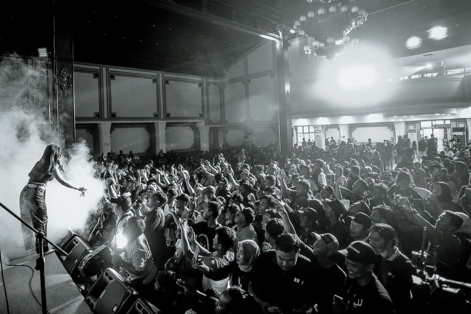 Wide shot of a silhouetted performer on stage facing a packed concert venue.