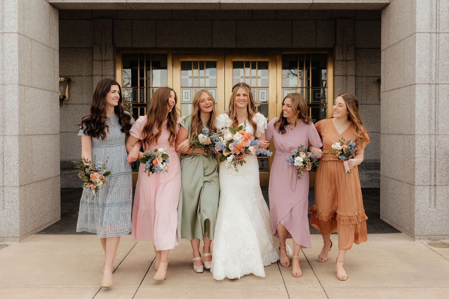 Bridesmaids and bride walking forward and laughing in front of gold doors