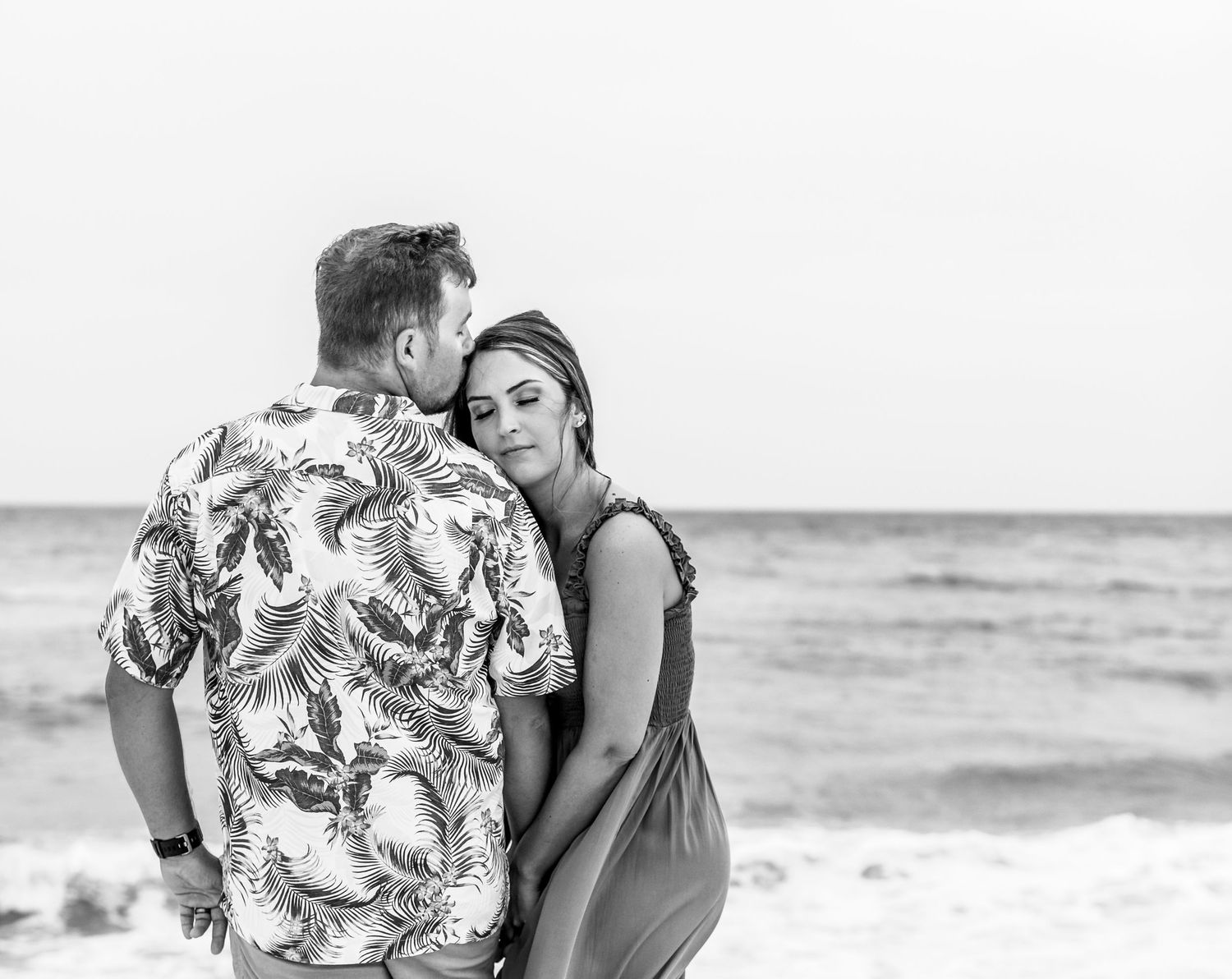 A romantic black and white portrait of a couple embracing on the beach.