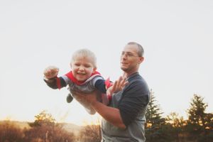 Adult lifts small child in red sweater during golden sunset outdoors.