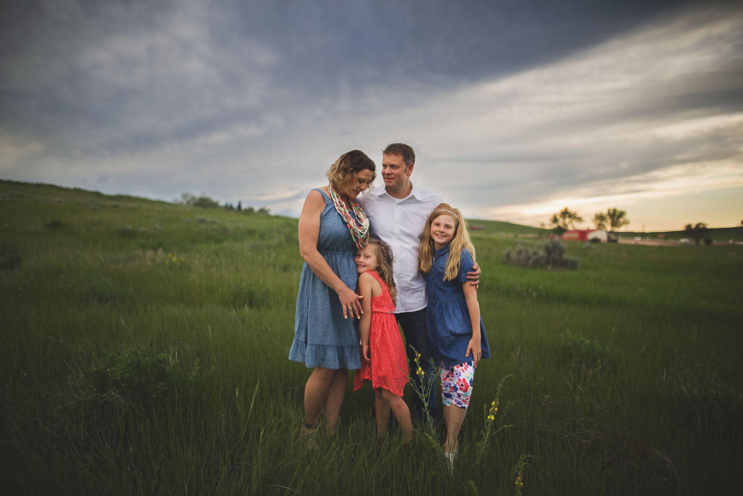 Family spending time together in a green field at sunset with dramatic clouds overhead.