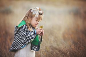 Young child in checkered cape examines leaf in autumn field.