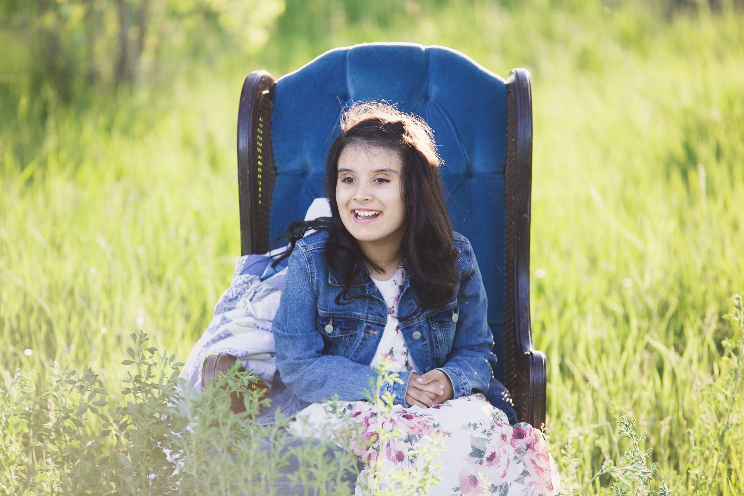 Person relaxes in blue vintage chair surrounded by tall grass and wildflowers.