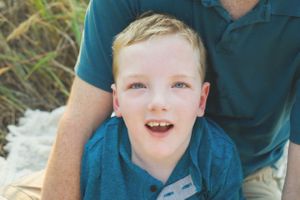 Close-up outdoor portrait showing bright smile and blue shirt against natural background.