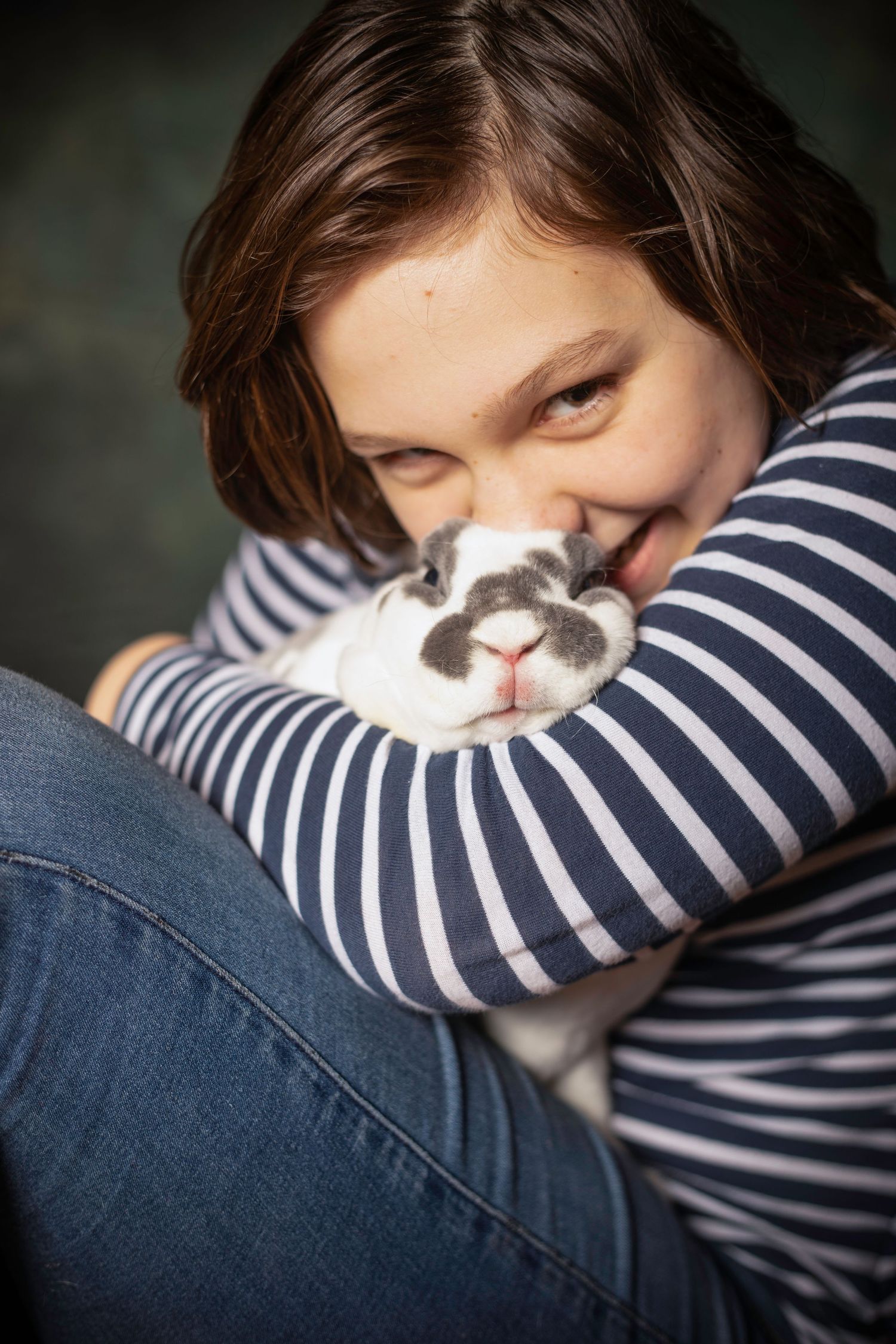 Person in striped shirt cuddling with a black and white rabbit.