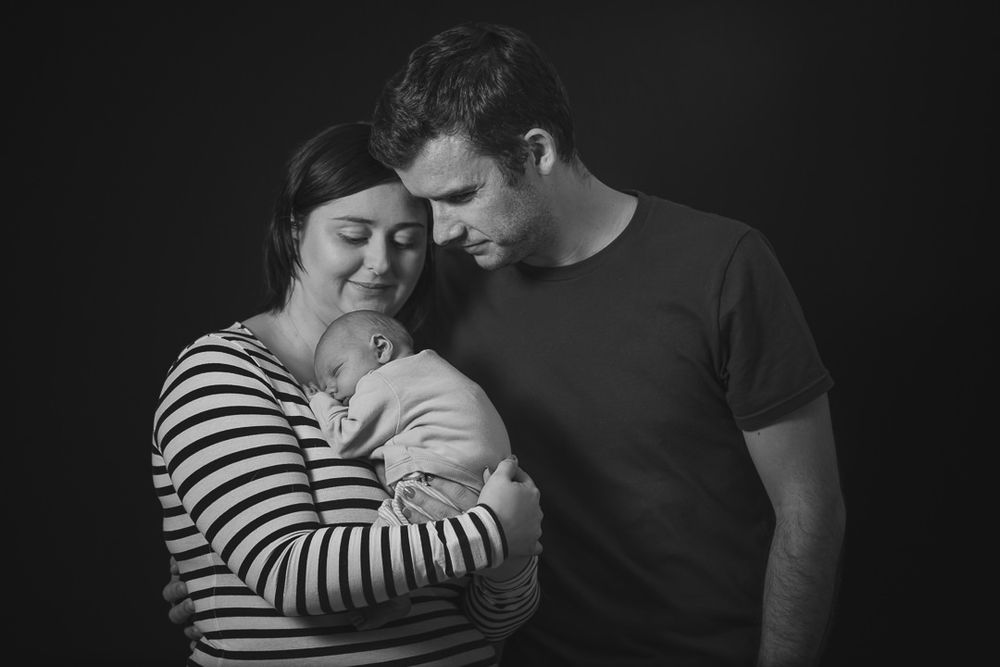 Black and white photo of a young couple with their newborn son. Mother cradling the baby.