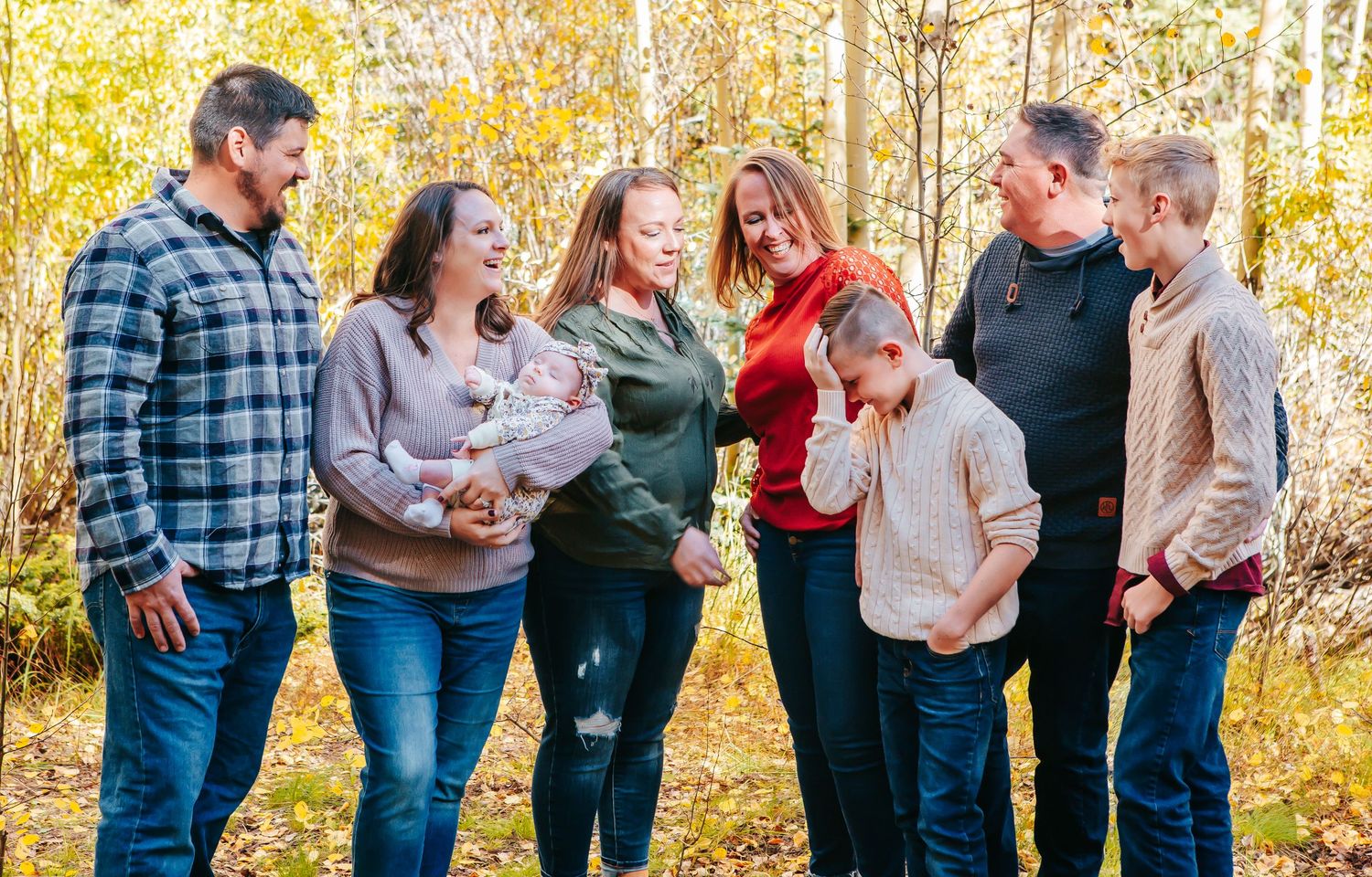 A happy family group laughs together while standing among autumn aspen trees.