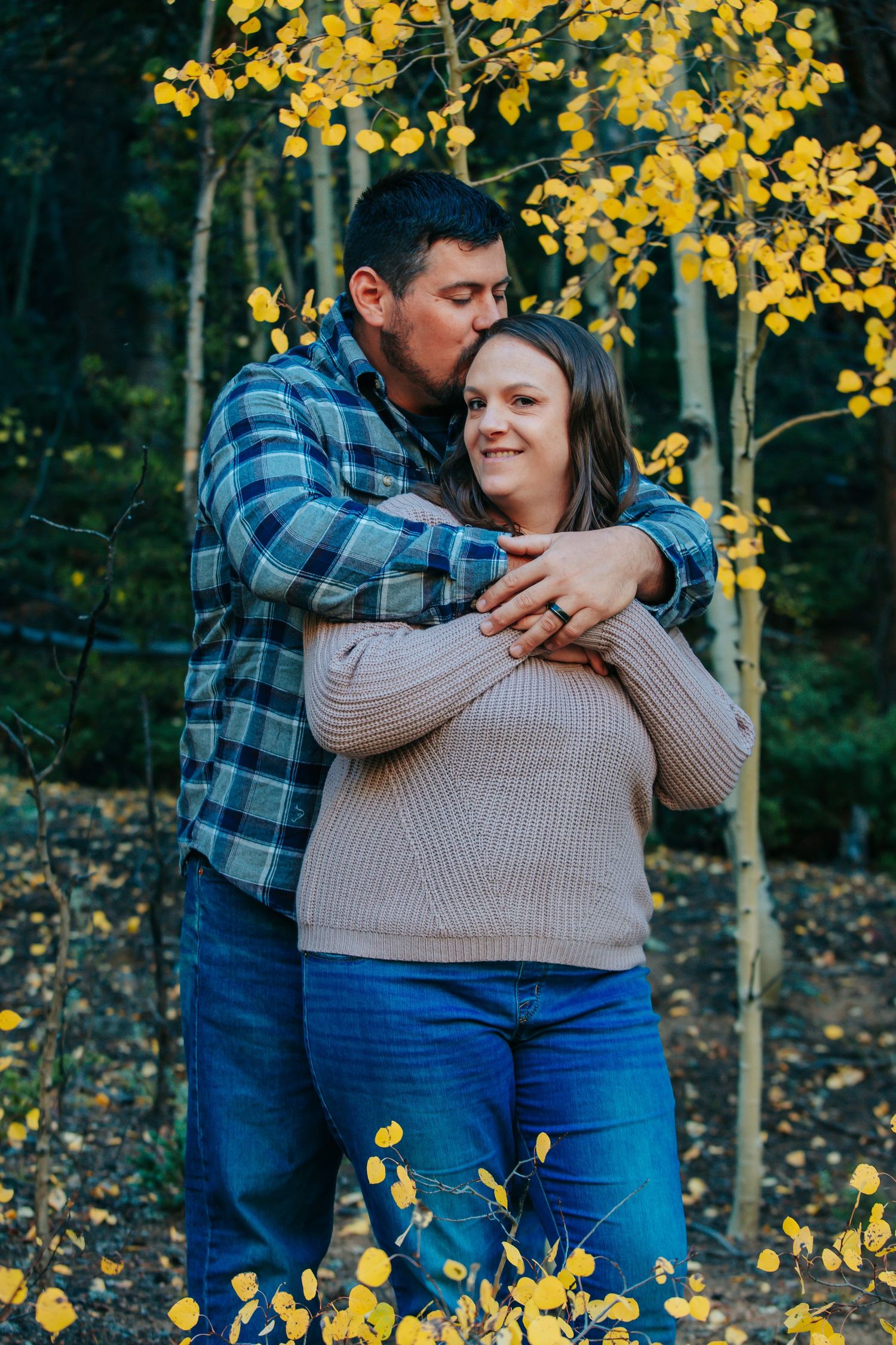 A romantic autumn portrait in the woods with golden aspen leaves framing a tender embrace.