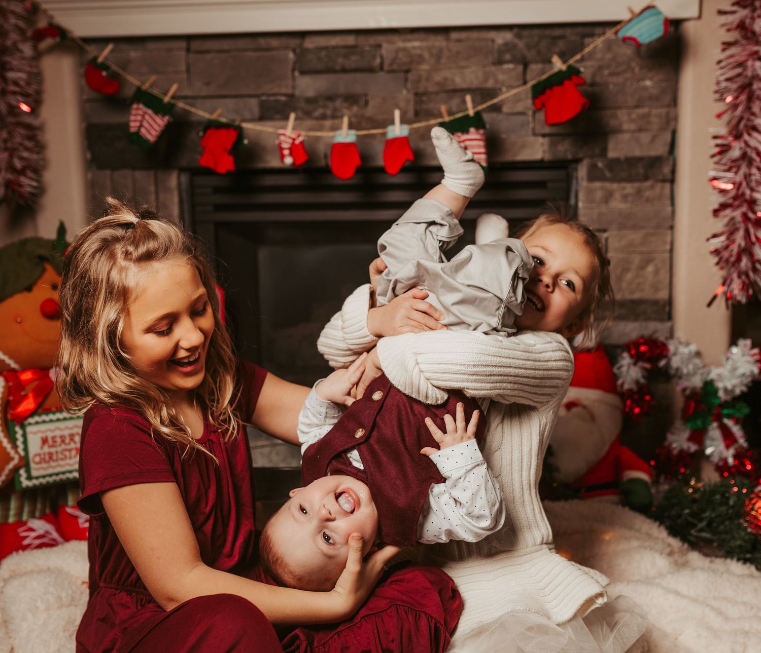 Family plays and laughs together by a fireplace decorated with Christmas stockings.