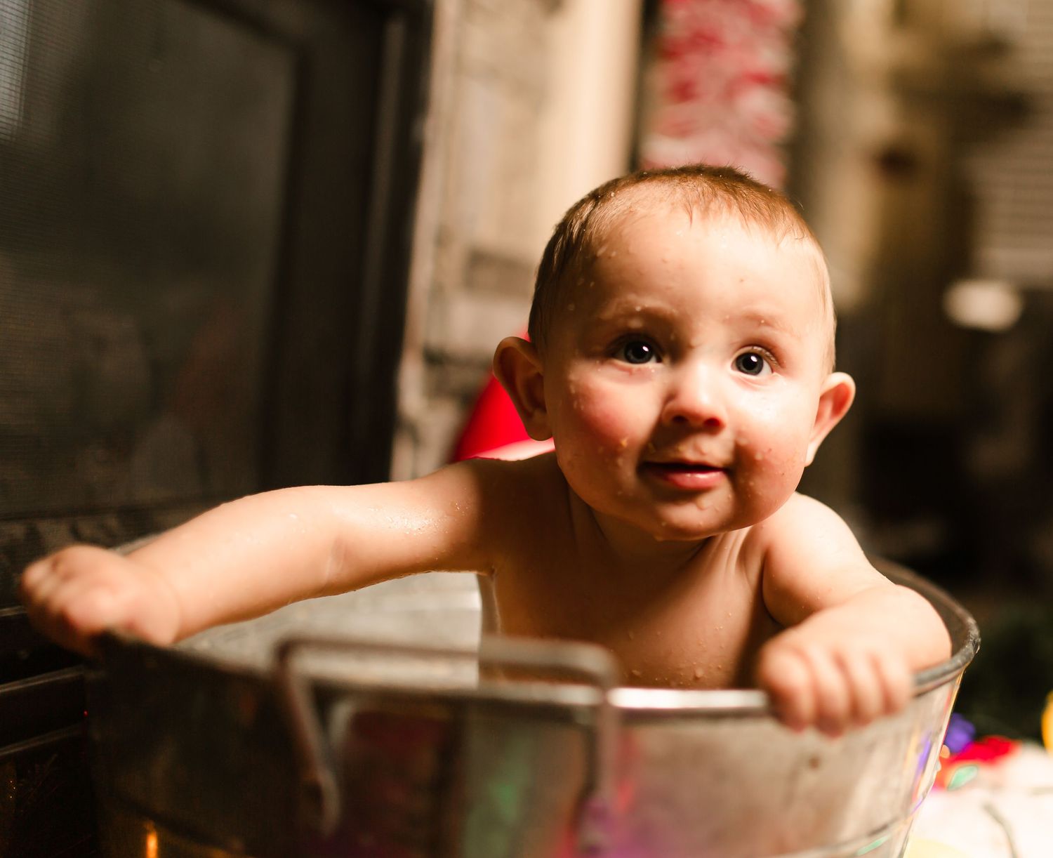 Smiling baby peeks out from inside a large metal mixing bowl.