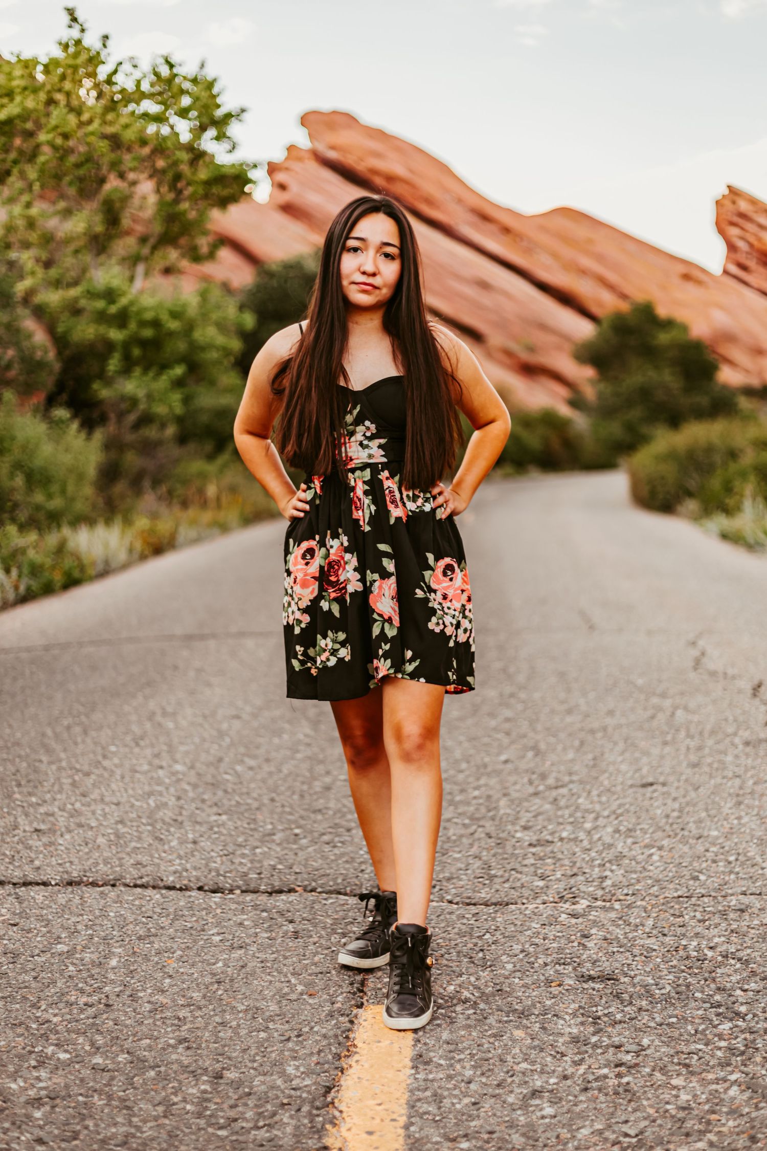 Woman in floral dress poses on road with dramatic red rock formations in background.