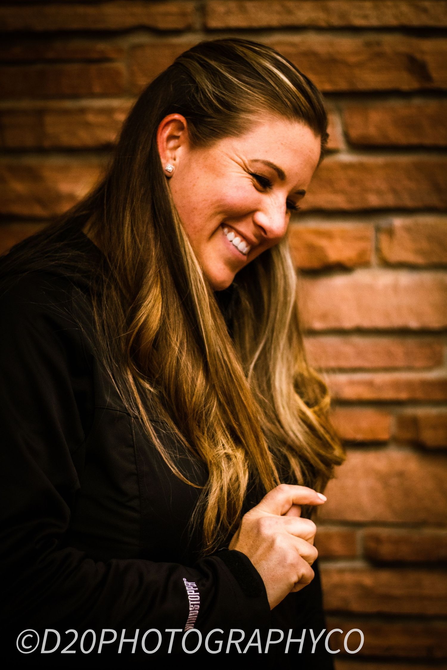 Portrait of woman smiling in black jacket against brick wall background.