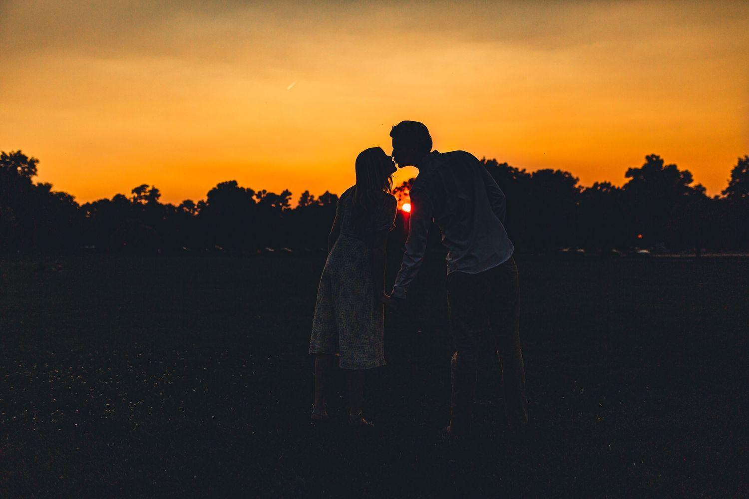 Romantic silhouette of couple against vibrant orange sunset sky.