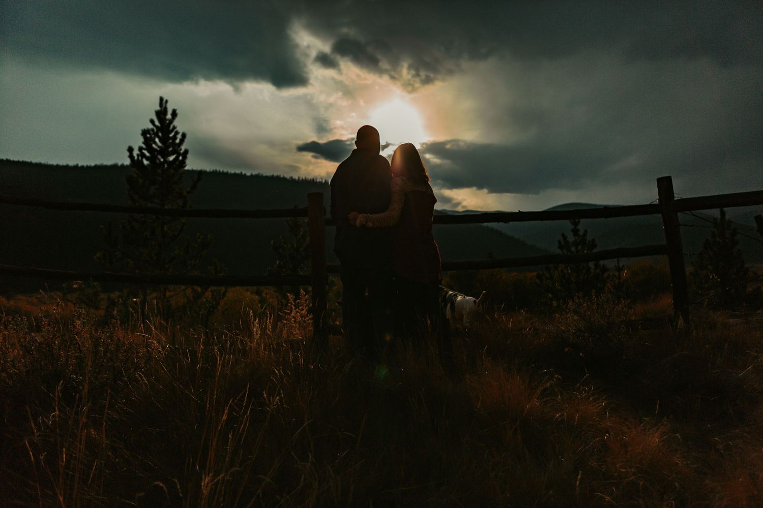 Silhouetted couple stands together against dramatic stormy sunset sky.