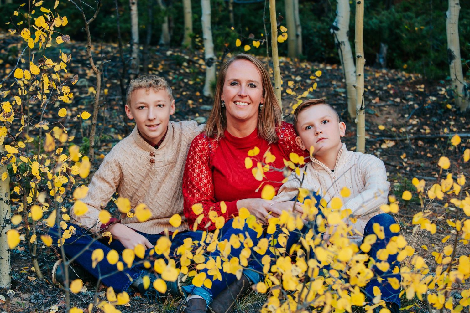 A family group poses beneath golden aspen leaves in autumn.