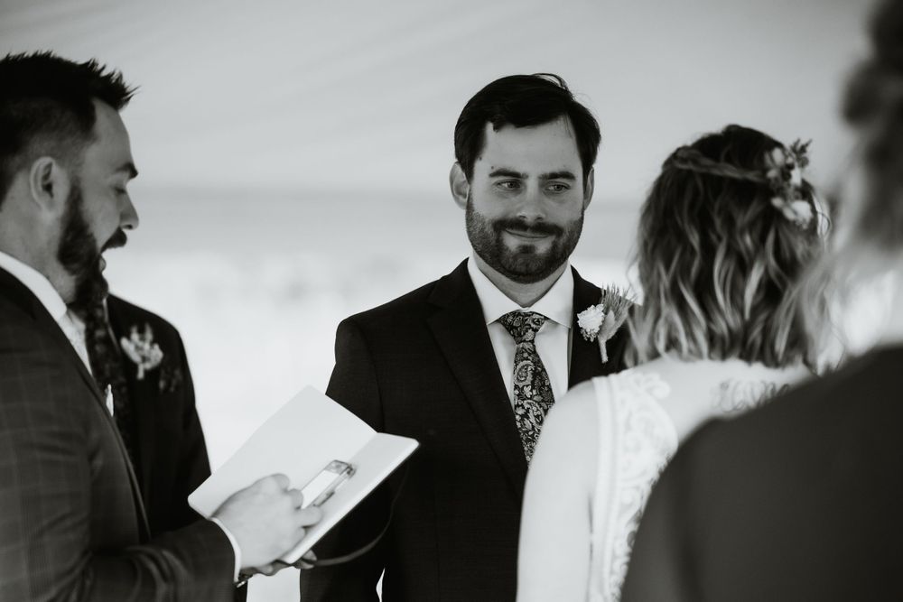 A wedding ceremony moment captured in black and white under a tent.
