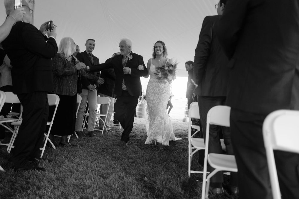 Wedding ceremony guests stand in rows of white chairs during an outdoor celebration.
