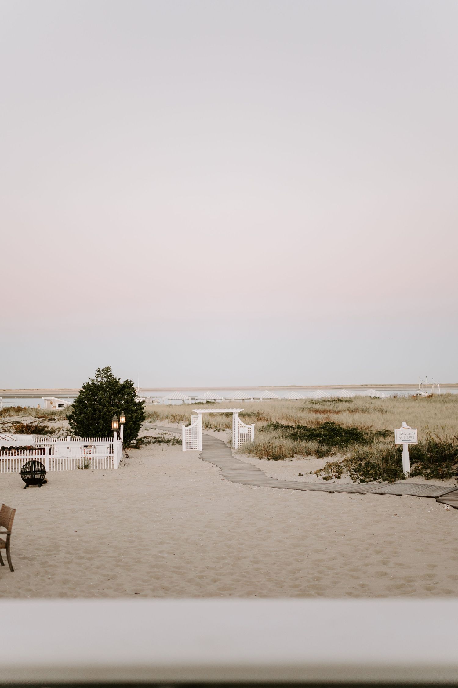 Serene beachfront landscape with white fencing and natural dunes at sunset.