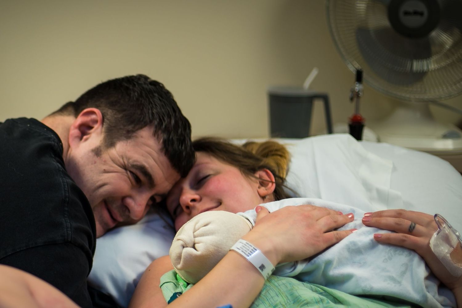 Proud dad looking at his new baby boy while his wife holds their son and rests just after birth in Sioux City, IA.