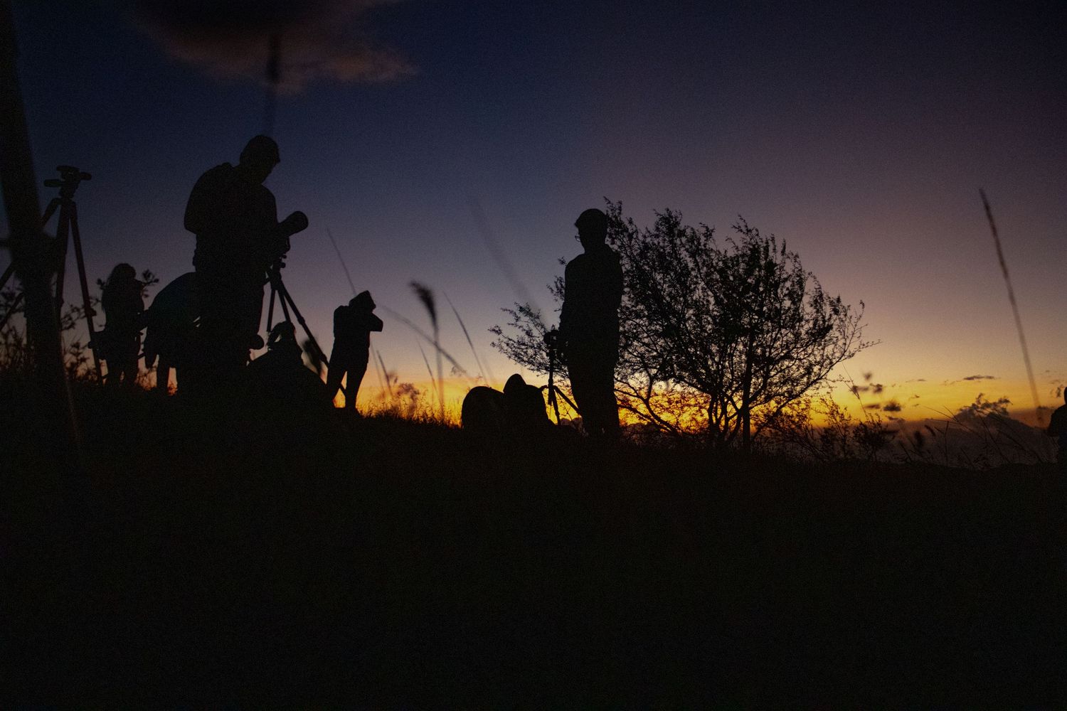 People silhouetted against a dramatic sunset sky while walking along a ridge.