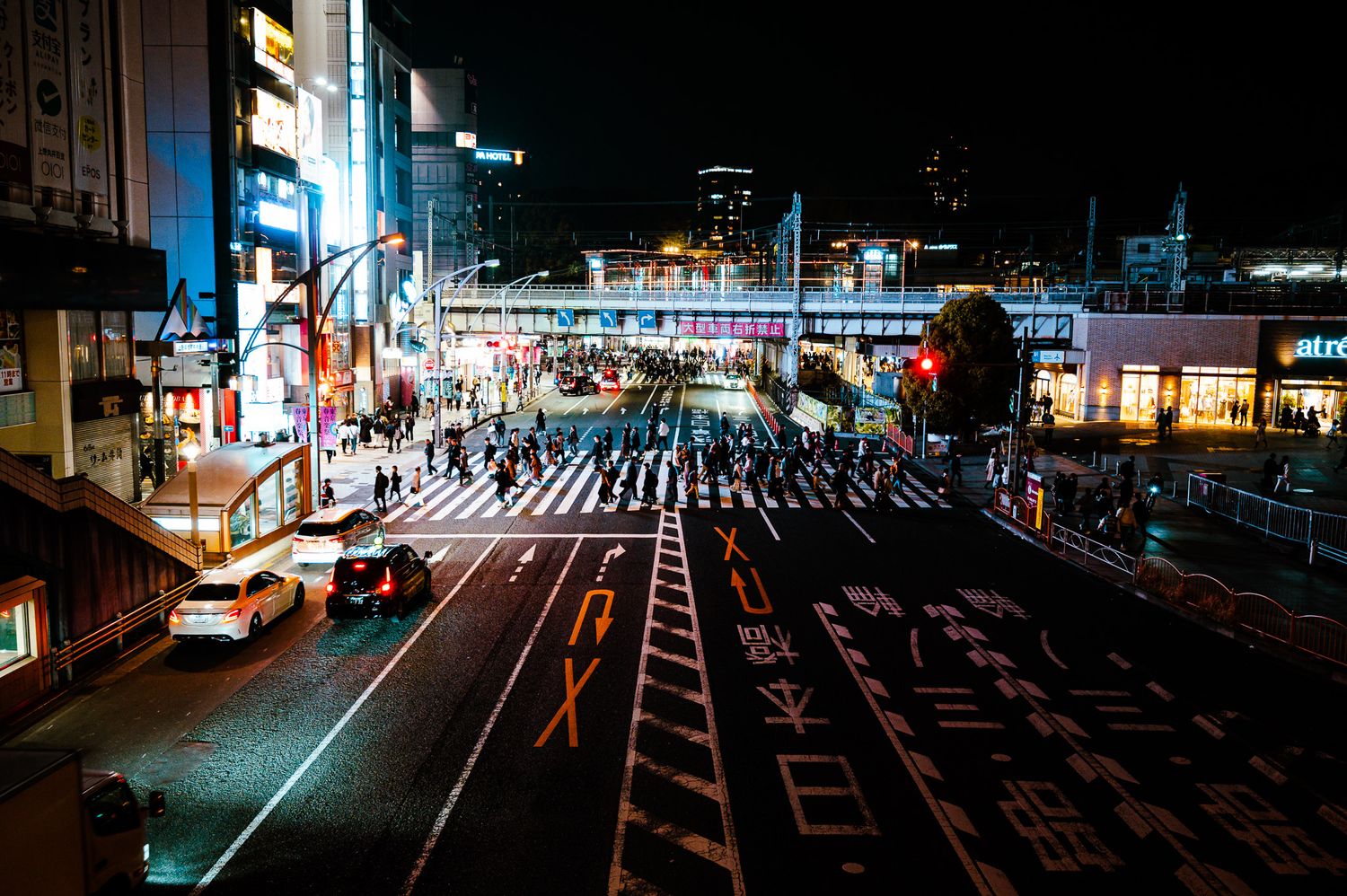 Illuminated Japanese city street at night with bright neon signs and crosswalk markings.