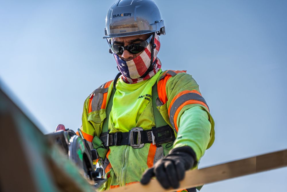Construction worker in protective equipment operating tools at elevated worksite.