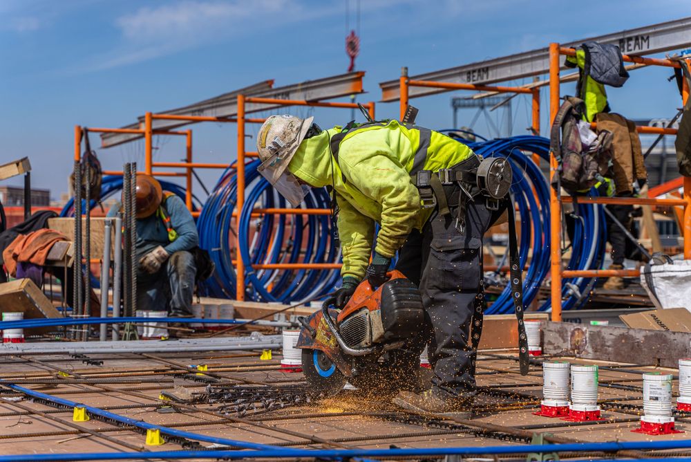 Construction workers installing rebar on commercial building site with blue safety barriers.
