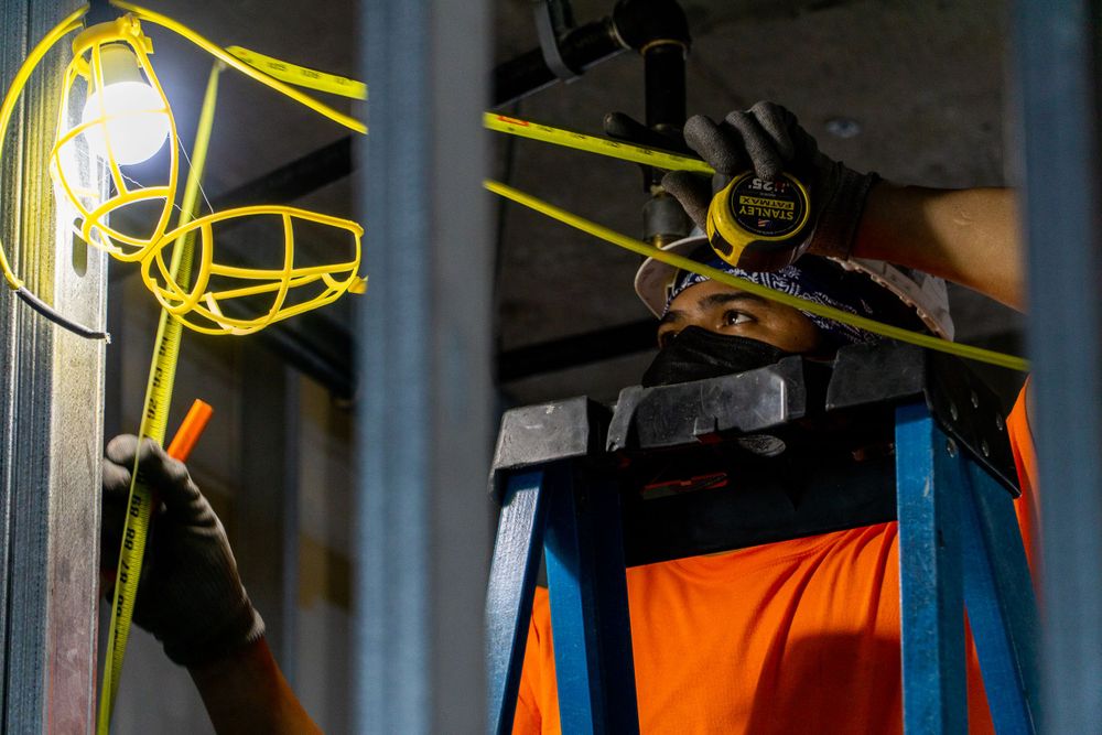 Yellow construction light fixture illuminated in dark industrial setting with orange safety equipment.
