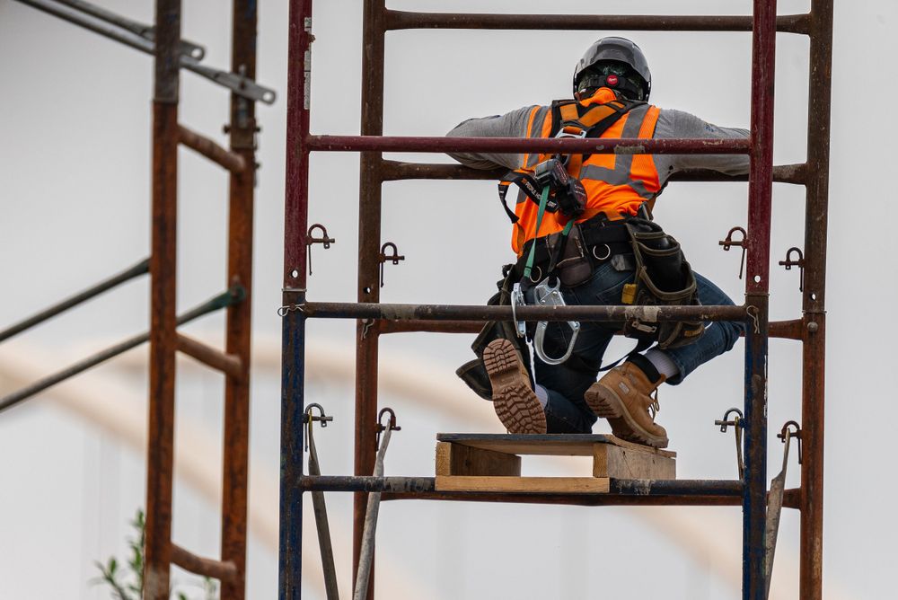 Construction worker in orange safety vest working on elevated scaffolding structure.