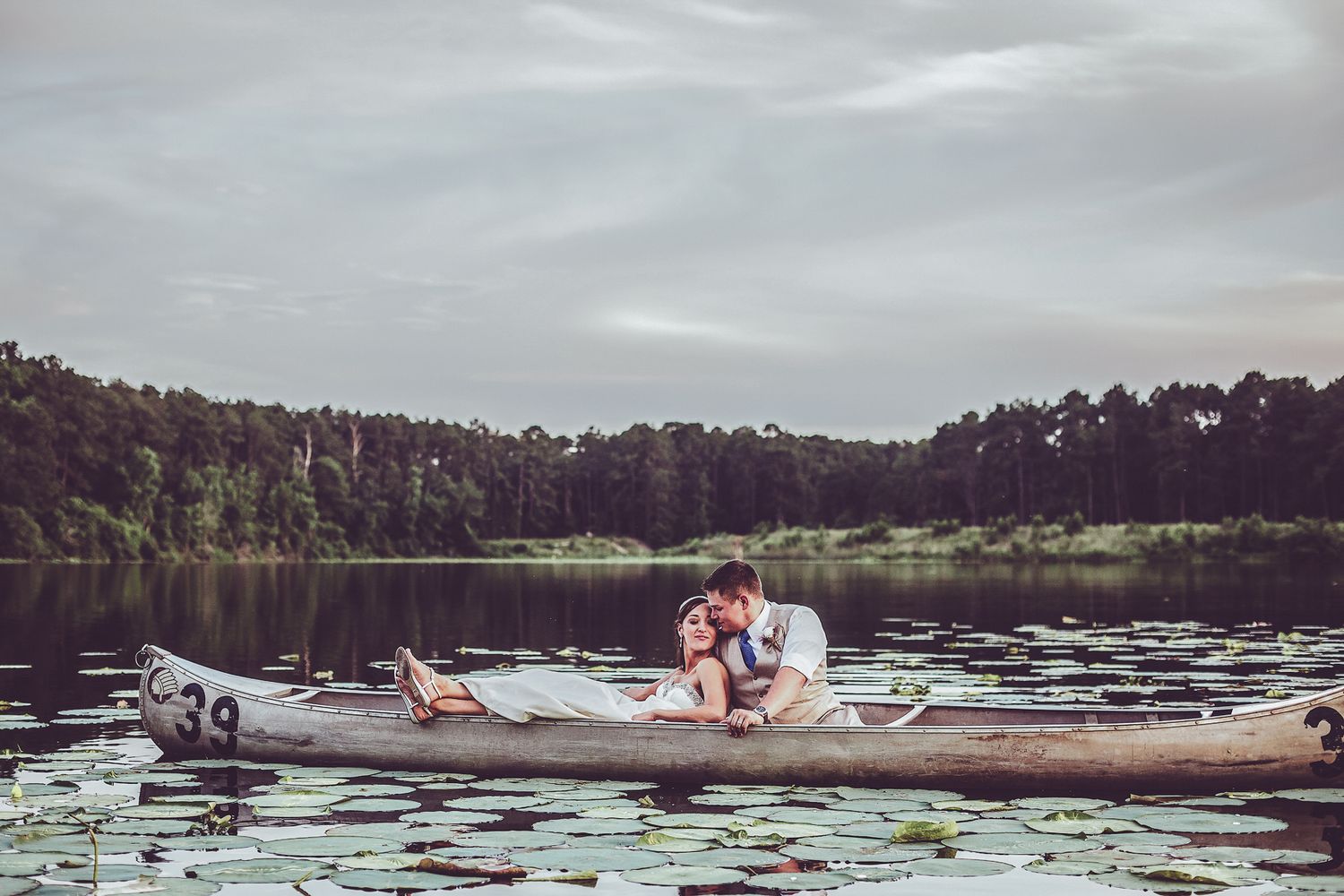 couple bride groom sitting in a canoe kissing with lily pads and pine trees