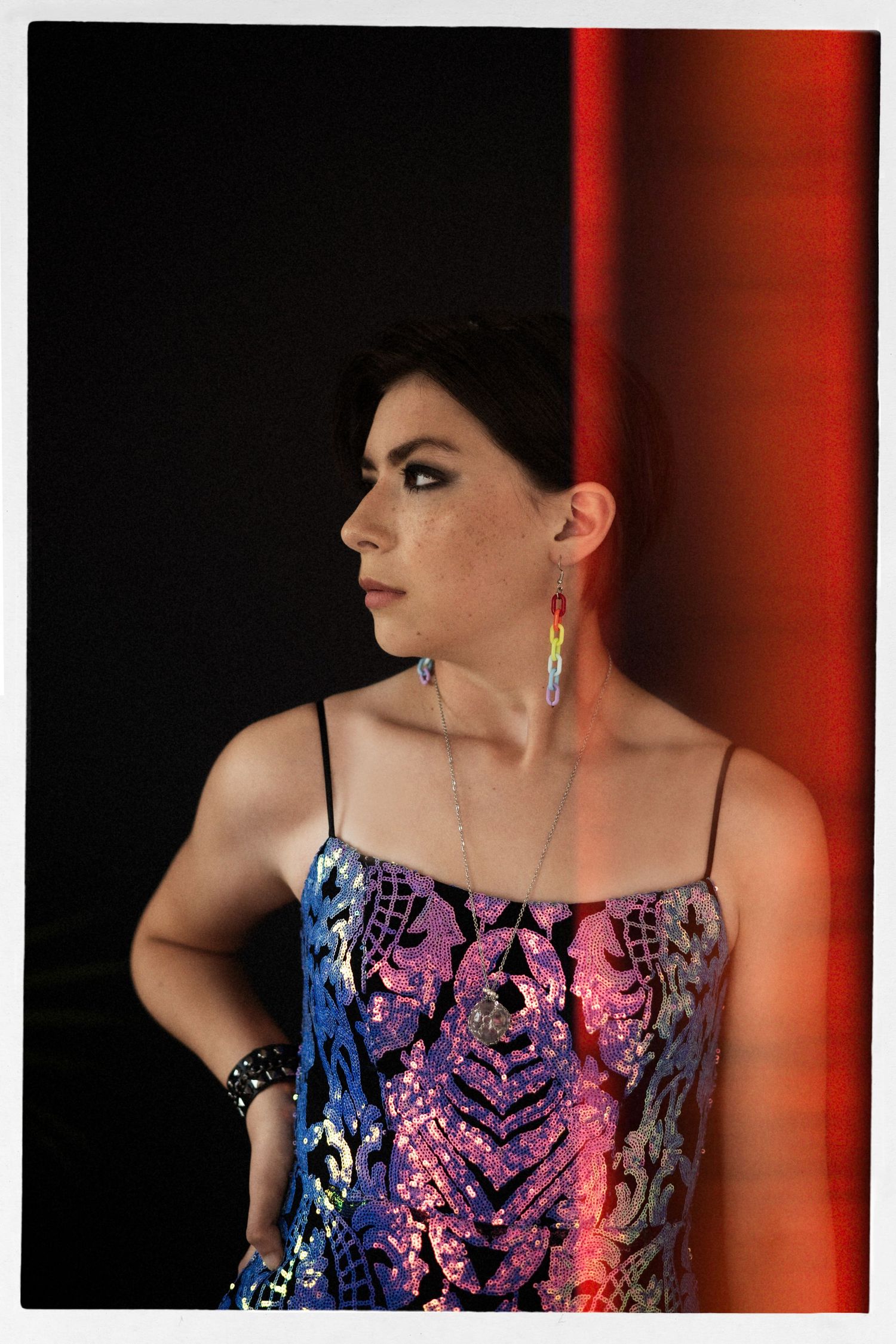 A dramatic portrait featuring a sequined dress with blue and pink tones against a red-lit background.