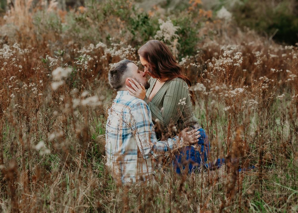 Romantic couple sharing a kiss while embracing in a golden wildflower meadow at sunset.